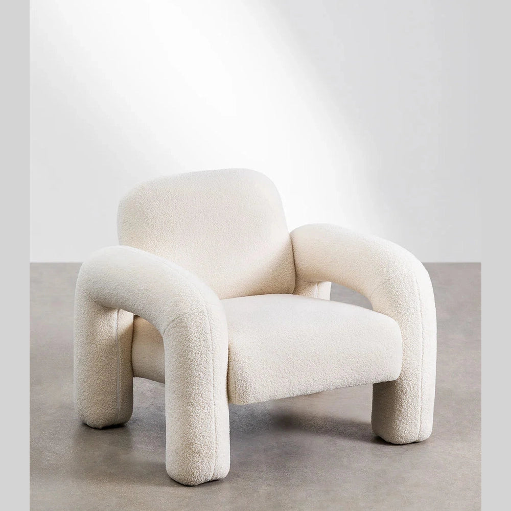 Fauteuil Alma au style minimaliste avec formes enveloppantes et revêtement doux effet laine bouclée.